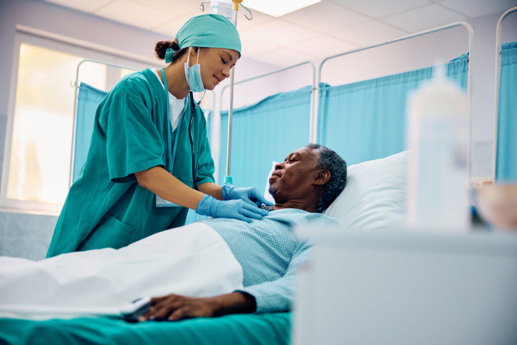Smiling nurse checking heartbeat of recovering black senior patient in hospital ward