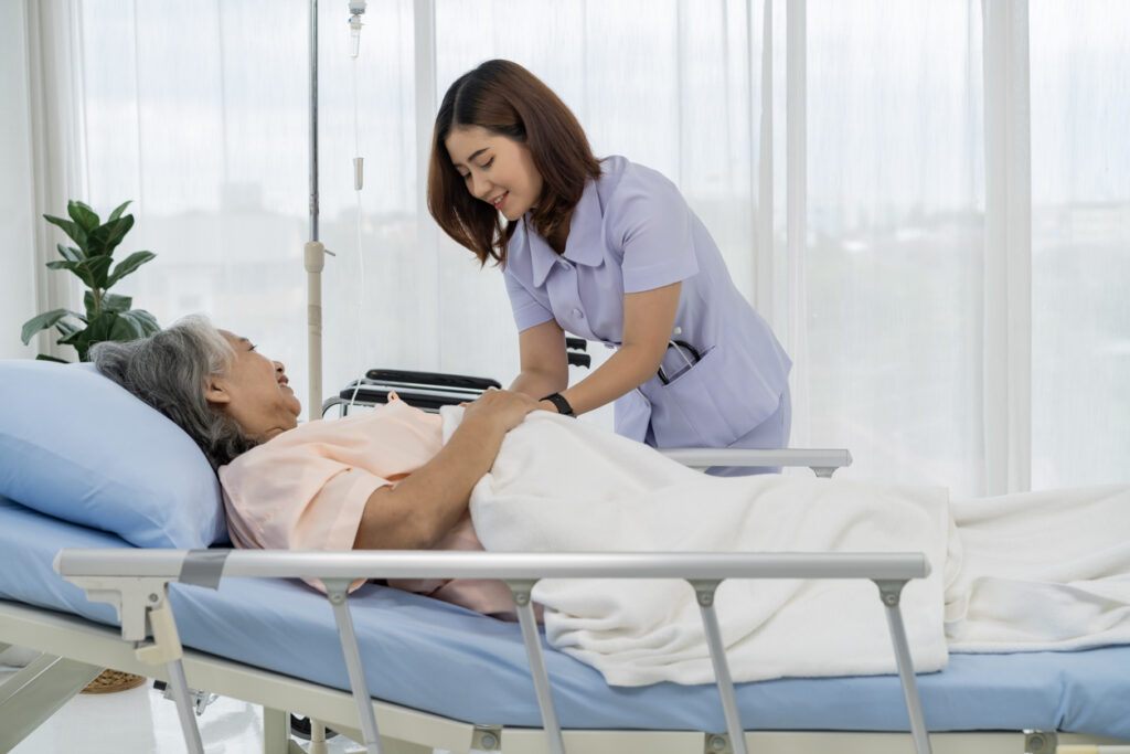 A nurse or caregiver of an elderly patient is helping to cover blanket a patient lying in bed